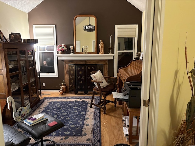 sitting room featuring a textured ceiling, light wood-type flooring, and vaulted ceiling