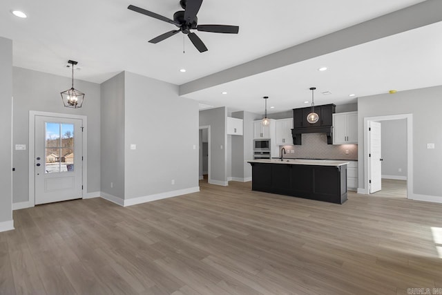 kitchen with ceiling fan with notable chandelier, backsplash, a center island with sink, and hanging light fixtures