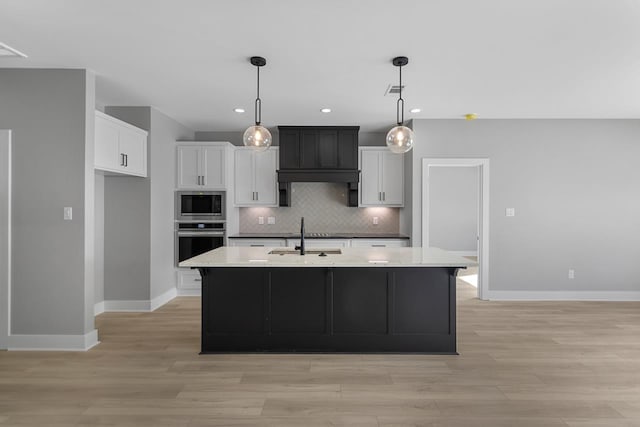 kitchen with appliances with stainless steel finishes, sink, white cabinets, and an island with sink