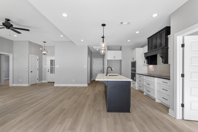 kitchen with a kitchen island with sink, sink, ceiling fan with notable chandelier, and white cabinetry