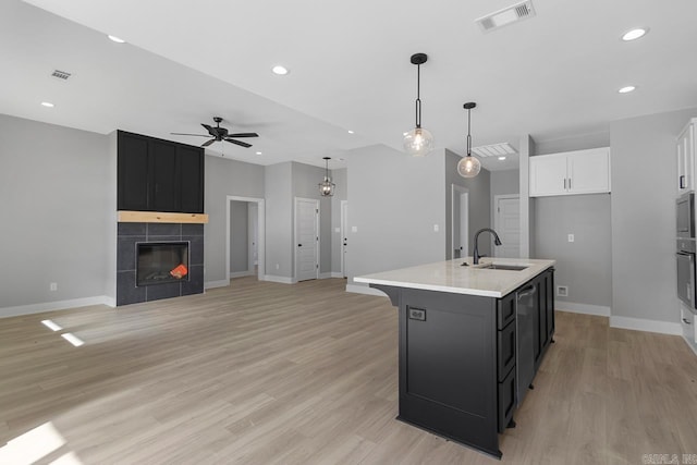 kitchen featuring ceiling fan, a fireplace, sink, a kitchen island with sink, and white cabinets