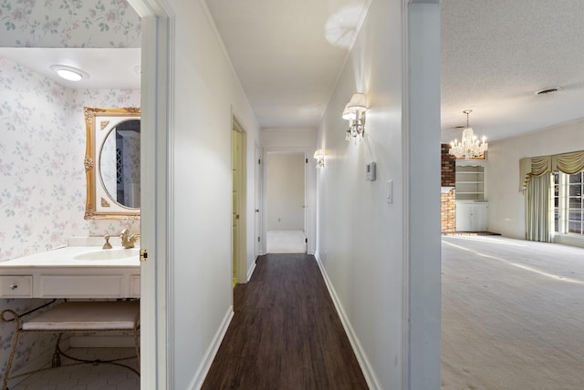 corridor with a textured ceiling, an inviting chandelier, dark hardwood / wood-style floors, and sink