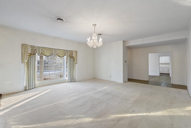 carpeted empty room featuring a textured ceiling and an inviting chandelier