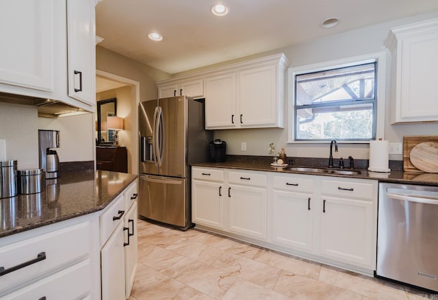 kitchen featuring appliances with stainless steel finishes, dark stone countertops, white cabinetry, and sink