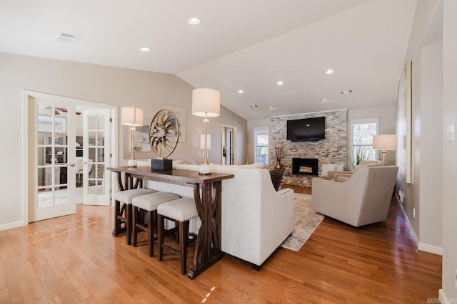 living room with vaulted ceiling, french doors, a stone fireplace, and hardwood / wood-style flooring