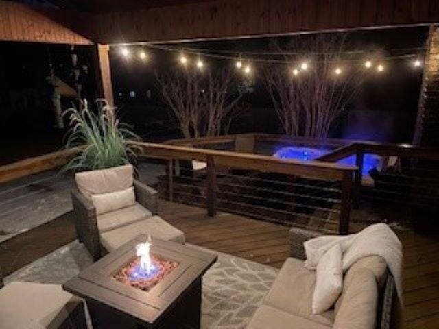 patio at night featuring a deck, a jacuzzi, and an outdoor living space with a fire pit