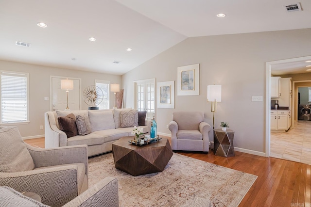 living room featuring washer / dryer, vaulted ceiling, and light hardwood / wood-style flooring