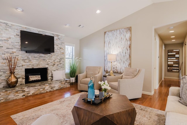 living room featuring light hardwood / wood-style flooring, lofted ceiling, and a stone fireplace