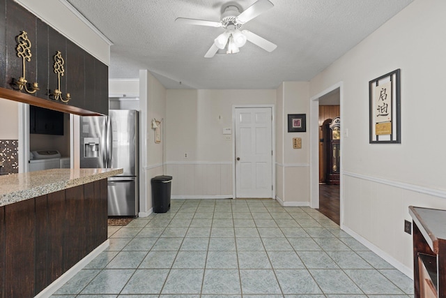 kitchen featuring stainless steel refrigerator with ice dispenser, ceiling fan, washer and dryer, light stone countertops, and a textured ceiling