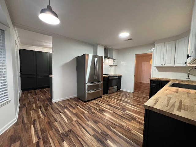 kitchen featuring appliances with stainless steel finishes, wall chimney exhaust hood, wood counters, white cabinetry, and tasteful backsplash