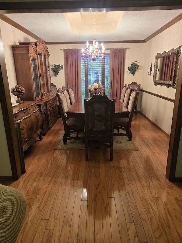 dining space with crown molding, wood-type flooring, an inviting chandelier, and a textured ceiling