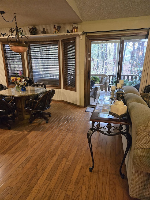 dining space with vaulted ceiling, a chandelier, a textured ceiling, and wood-type flooring