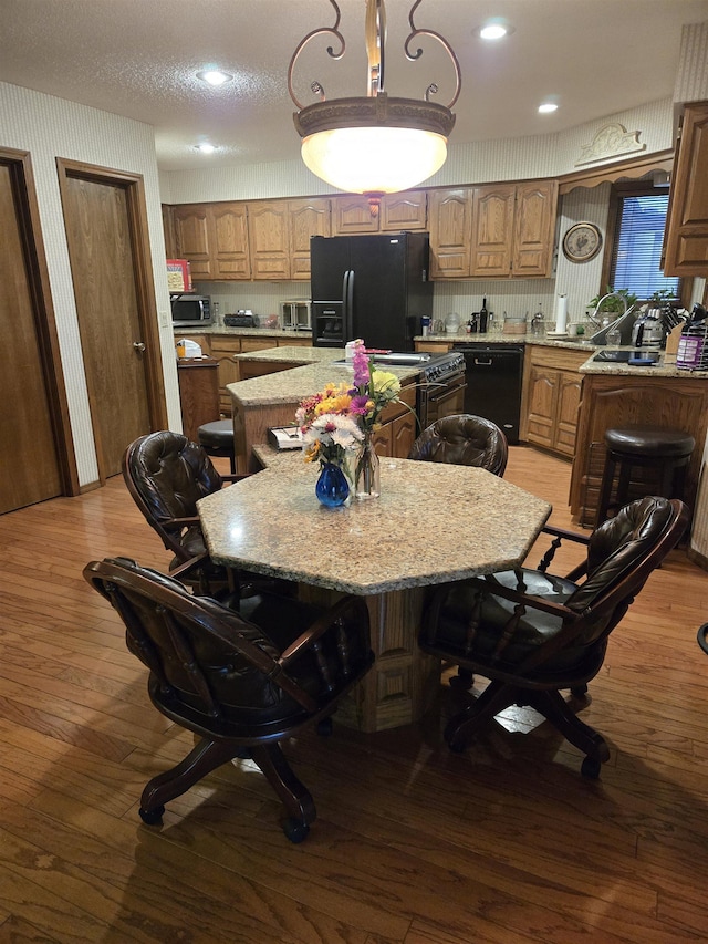 kitchen featuring a textured ceiling, black appliances, a kitchen island, light stone counters, and light hardwood / wood-style flooring