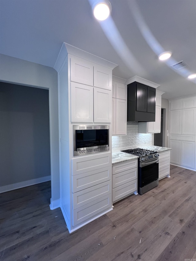 kitchen with white cabinetry, wood-type flooring, appliances with stainless steel finishes, light stone countertops, and backsplash