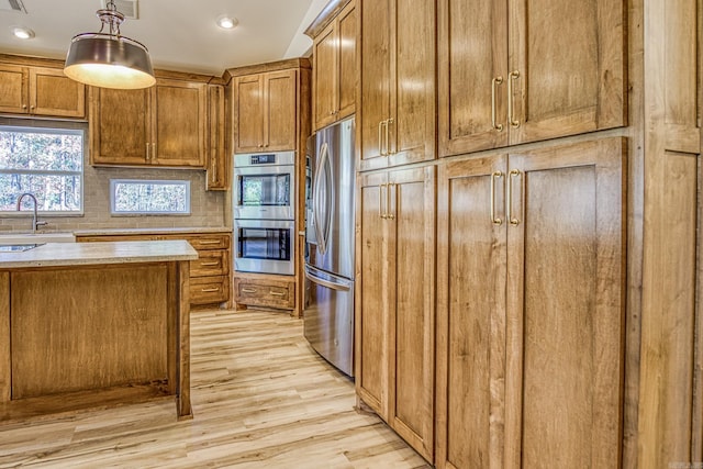 kitchen with appliances with stainless steel finishes, tasteful backsplash, light wood-type flooring, hanging light fixtures, and sink