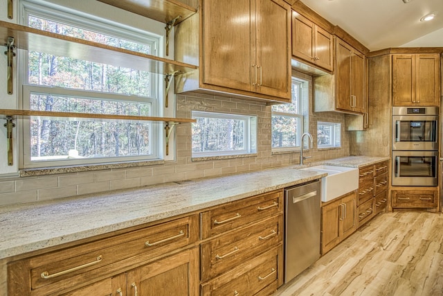 kitchen with light hardwood / wood-style floors, a wealth of natural light, sink, appliances with stainless steel finishes, and light stone counters