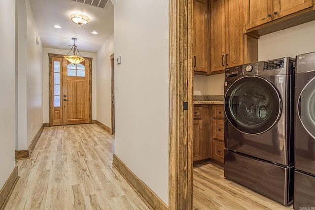 clothes washing area with washer and dryer, cabinets, and light hardwood / wood-style floors