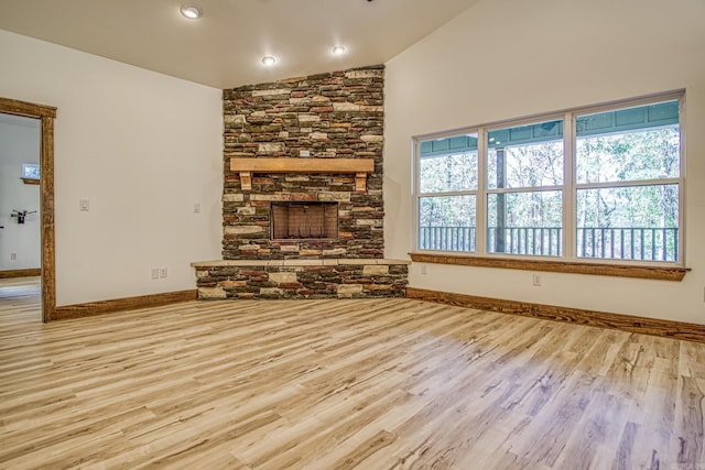 unfurnished living room featuring lofted ceiling, light wood-type flooring, and a stone fireplace