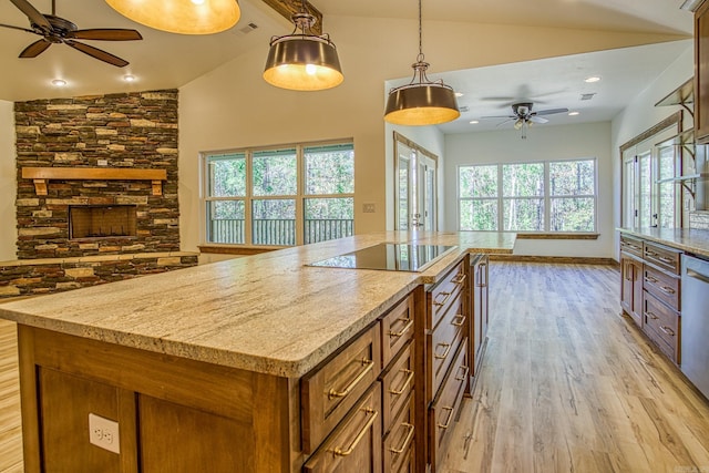 kitchen with light stone counters, light hardwood / wood-style flooring, black electric cooktop, and hanging light fixtures