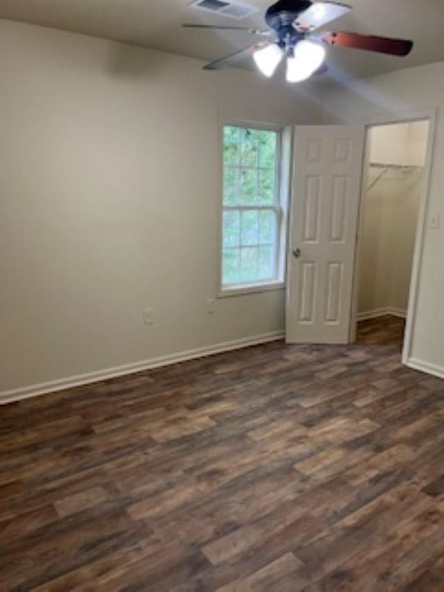 unfurnished bedroom with ceiling fan, a spacious closet, a closet, and dark wood-type flooring