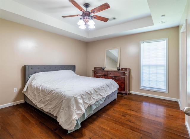 bedroom featuring ceiling fan, dark wood-type flooring, and a tray ceiling