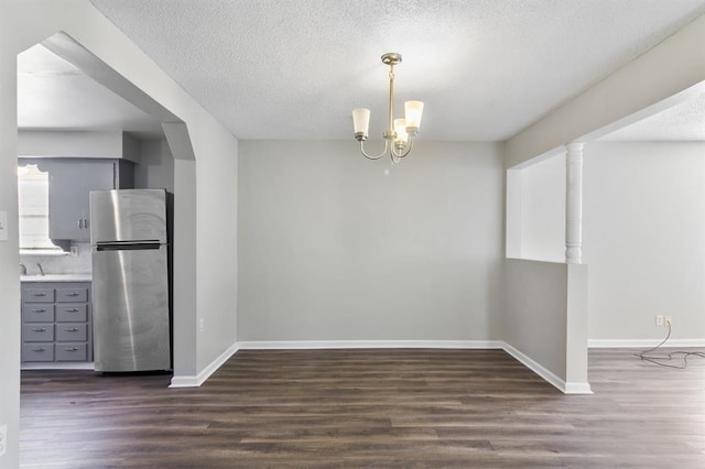 unfurnished dining area with a textured ceiling, an inviting chandelier, and dark hardwood / wood-style floors