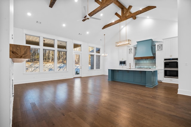 kitchen with custom exhaust hood, white cabinetry, hanging light fixtures, an island with sink, and backsplash