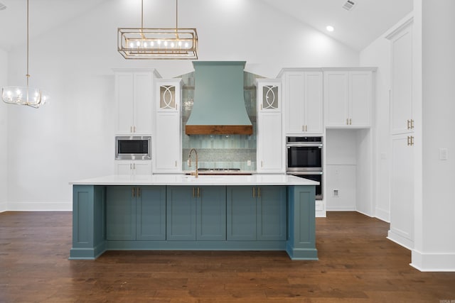 kitchen featuring appliances with stainless steel finishes, custom range hood, a kitchen island with sink, and decorative light fixtures