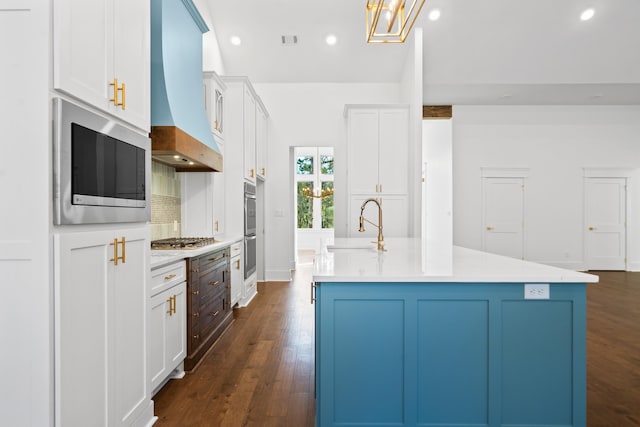 kitchen featuring premium range hood, sink, a center island with sink, stainless steel appliances, and white cabinets