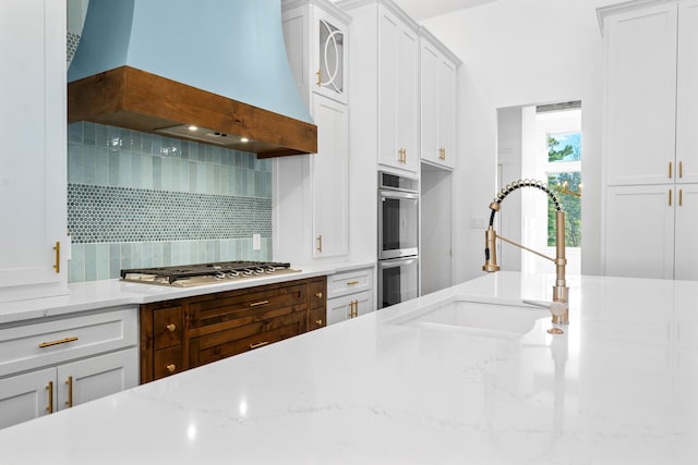 kitchen with sink, appliances with stainless steel finishes, white cabinetry, backsplash, and custom range hood