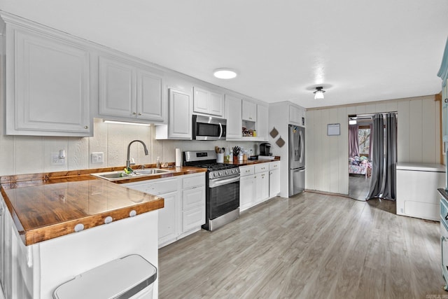 kitchen featuring white cabinetry, butcher block counters, stainless steel appliances, light hardwood / wood-style floors, and sink