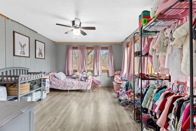 bedroom with ceiling fan, wood walls, a textured ceiling, and light hardwood / wood-style flooring