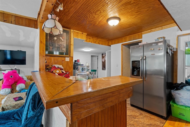 kitchen featuring stainless steel fridge with ice dispenser, kitchen peninsula, wood walls, and wooden ceiling