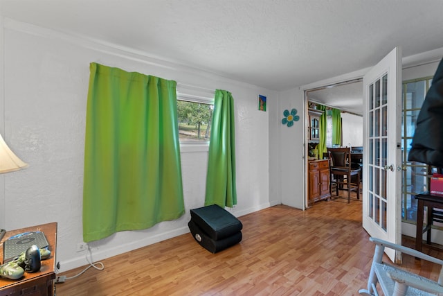 living area with a textured ceiling, light hardwood / wood-style flooring, and french doors