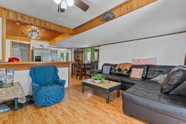 living room with wood walls, ceiling fan, and light hardwood / wood-style flooring