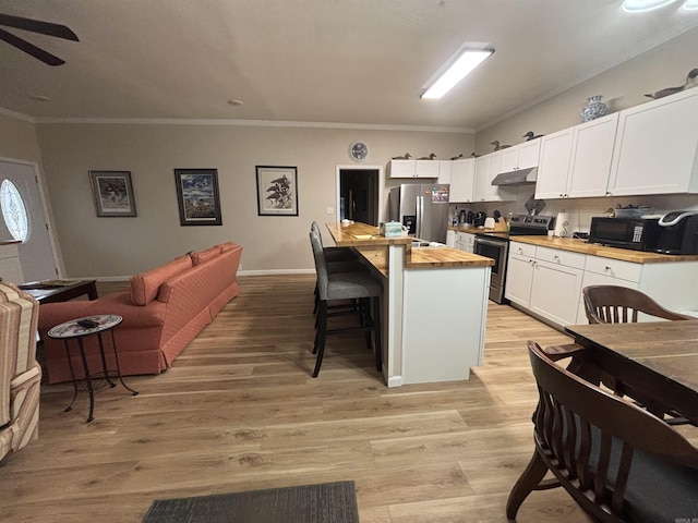 kitchen featuring white cabinets, butcher block countertops, a kitchen bar, and appliances with stainless steel finishes