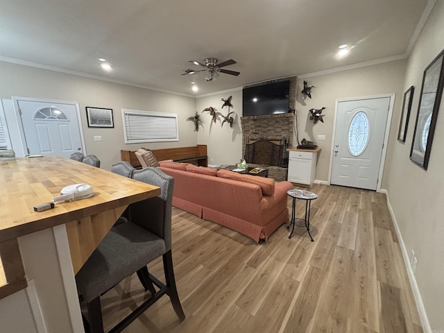 living room with light wood-type flooring, a brick fireplace, crown molding, and ceiling fan