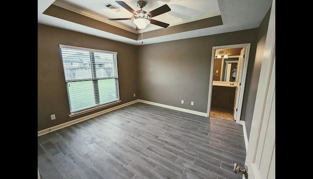 spare room featuring dark wood-type flooring, ceiling fan, ornamental molding, and a raised ceiling