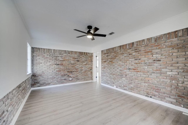 empty room with ceiling fan, brick wall, a textured ceiling, and light wood-type flooring