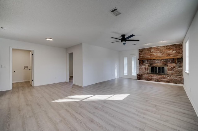 unfurnished living room with a brick fireplace, a textured ceiling, light hardwood / wood-style flooring, and ceiling fan