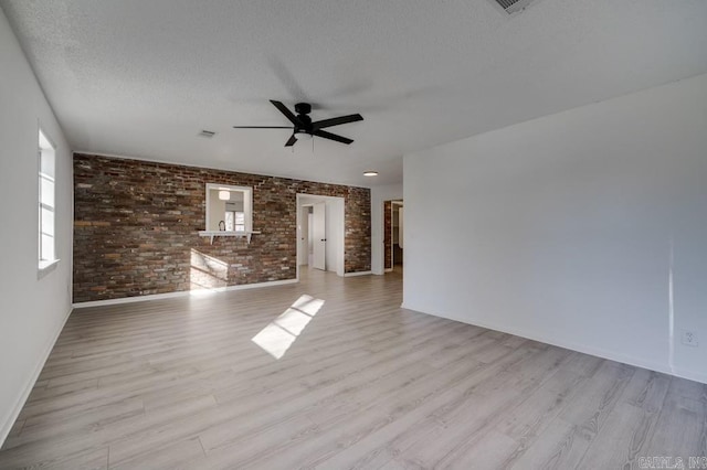 unfurnished room featuring ceiling fan, light wood-type flooring, brick wall, and a textured ceiling