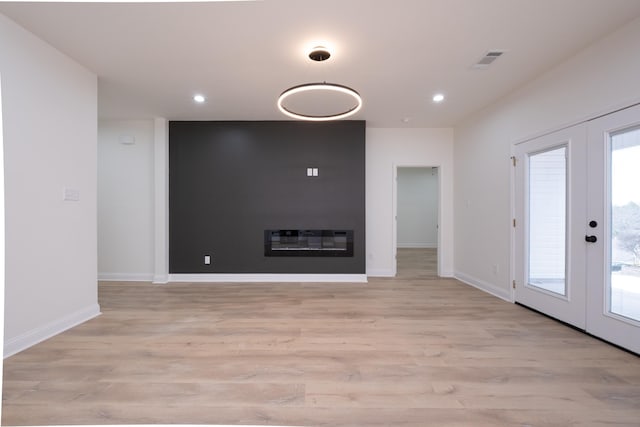 unfurnished living room featuring french doors, a large fireplace, and light hardwood / wood-style flooring