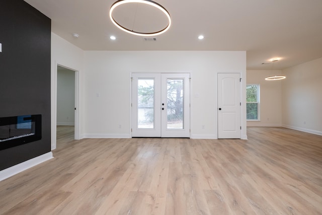 unfurnished living room featuring light hardwood / wood-style floors, a fireplace, french doors, and a healthy amount of sunlight