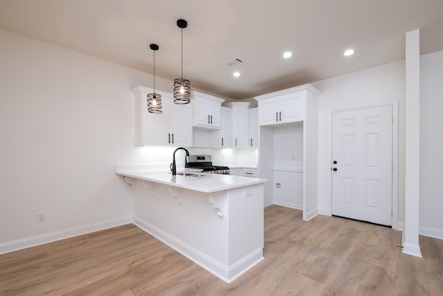 kitchen featuring decorative light fixtures, a kitchen bar, sink, white cabinetry, and light hardwood / wood-style flooring