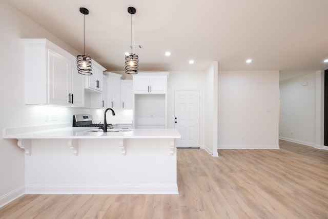 kitchen with a kitchen bar, sink, white cabinetry, hanging light fixtures, and light wood-type flooring