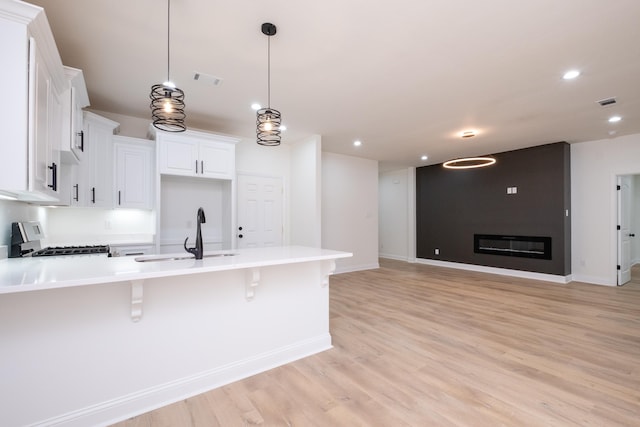 kitchen with white cabinets, gas stove, decorative light fixtures, sink, and a kitchen breakfast bar