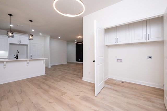 kitchen with white cabinets, decorative light fixtures, sink, light wood-type flooring, and a breakfast bar