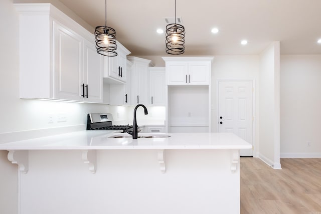 kitchen with pendant lighting, white cabinetry, stainless steel gas stove, sink, and a breakfast bar area