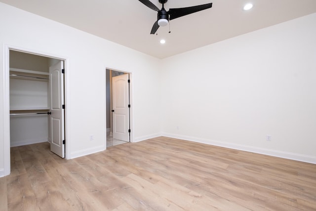 unfurnished bedroom with ceiling fan, a closet, a walk in closet, and light wood-type flooring