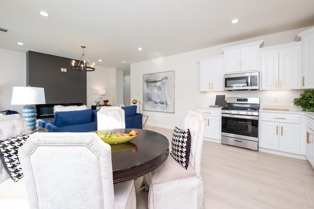 kitchen featuring white cabinets, decorative light fixtures, stainless steel appliances, a notable chandelier, and light wood-type flooring